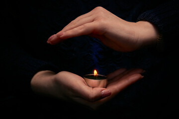 Close-up of female hands holding a burning candle in the dark. Selective focus