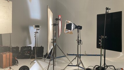 Wide view of filming equipment, lights, stands and flags, at a studio with white walls