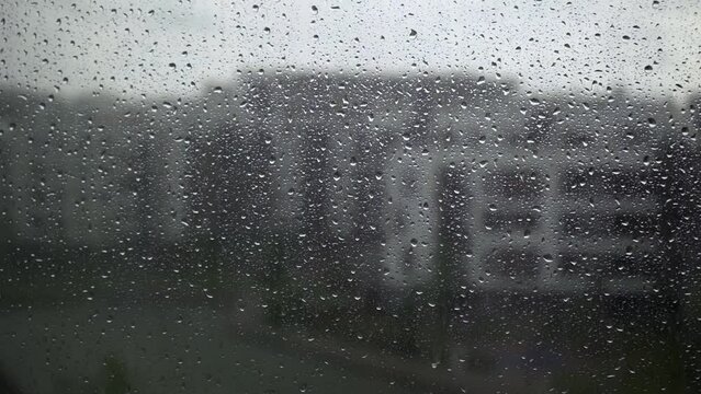 It is raining heavily outside the window, and transparent drops are flowing down the window pane. The city during the summer rain.