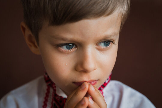 A little boy prays to God with his hands tucked open with his eyes open.