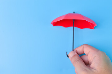Hand holding red toy umbrella isolated on a blue background