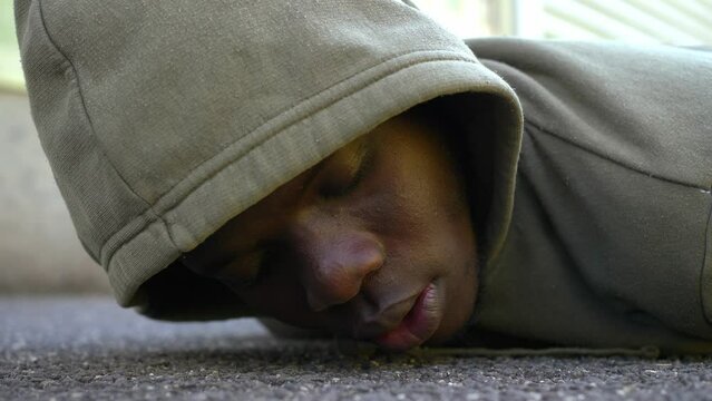 protest symbol - hooded black man lying on the ground stares at camera