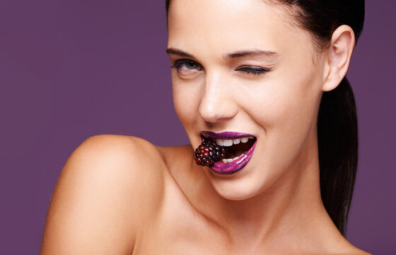 Berry Berry Nice. A Studio Portrait Of A Beautiful Young Woman Wearing Purple Lipstick And Biting Into A Berry.