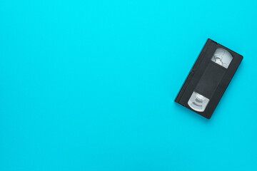 Old black videocassette flat lay top-down composition. Retro video tape over turquoise blue background with copy space.
