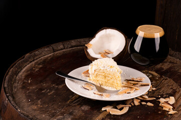 slice of coconut cake with dark stout beer over burnt coconut chips on rustic wood.