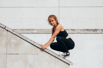 Parkour woman climbs the building and looks into the camera. Woman doing parkour in the city on a...