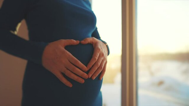 woman pregnant. motherhood a pregnancy sunset concept. 40 year old pregnant woman stands in a dress by the window holding her stomach silhouette. silhouette of a girl in by the window
