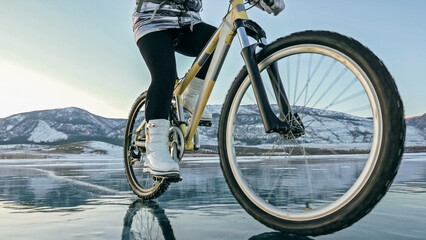 Woman is riding bicycle on the ice. Girl is dressed in a silvery down jacket, cycling backpack and...