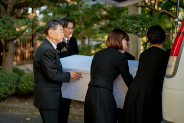 お葬式で棺桶を運ぶ遺族
