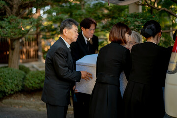 お葬式で棺桶を運ぶ遺族
