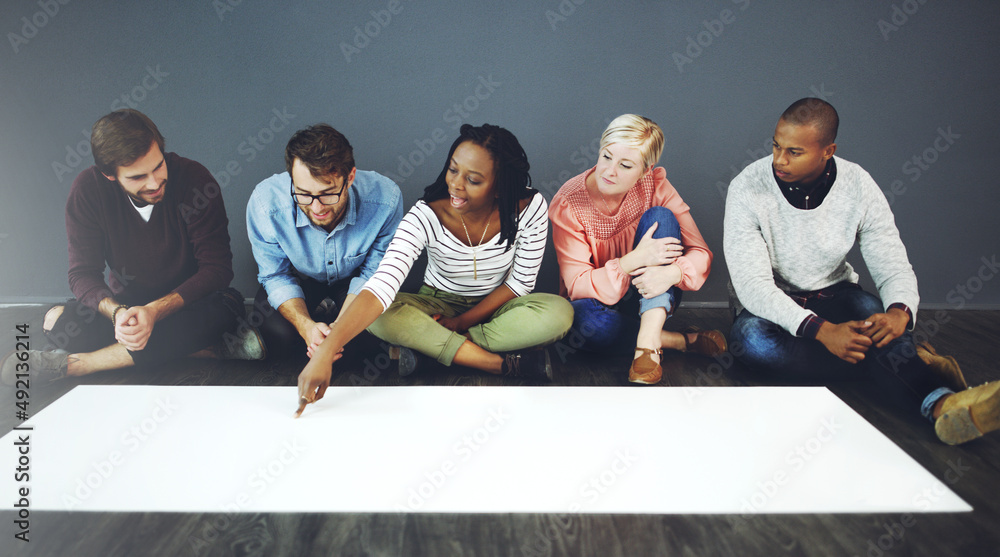 Poster Big paper for a big plan. Studio shot of a group of people sitting on the floor and working on blank paper against a gray background.