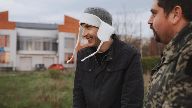 Two men met on the street and talking and laughing. One man in an shapka and the other in a military jacket. Comic images. Emotional conversation