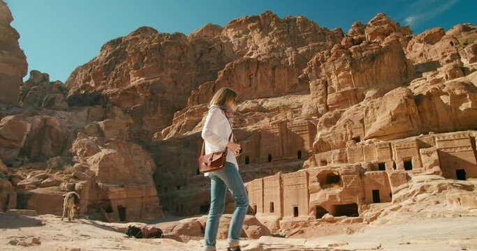 Female tourist visits Petra taking photo of ancient caves carved out of rock face. Most popular travel destination in Jordan, Middle East. Woman explore famous world heritage. 4K tracking gimbal shot