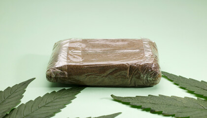 large portion hashish tablet with marijuana leaf, green background - obrazy, fototapety, plakaty