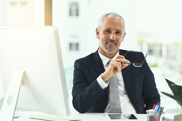 Taking my company to the top. Portrait of a smiling mature businessman sitting at his desk in an office.