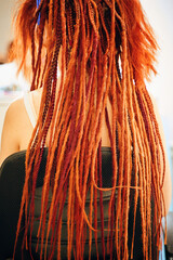 View from back of girl with red and orange dreadlocks from kanekalon. Stylish hairstyle of woman sitting in barber's chair.