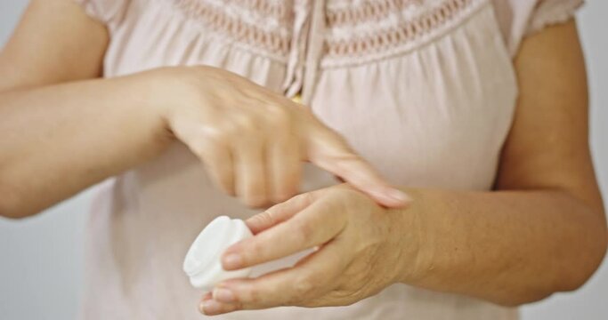 Older Woman Applies Cream On Her Hands Close-up On White Wooden Background.