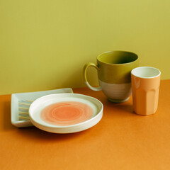 Empty plate and mug cup on orange table. yellow green wall background