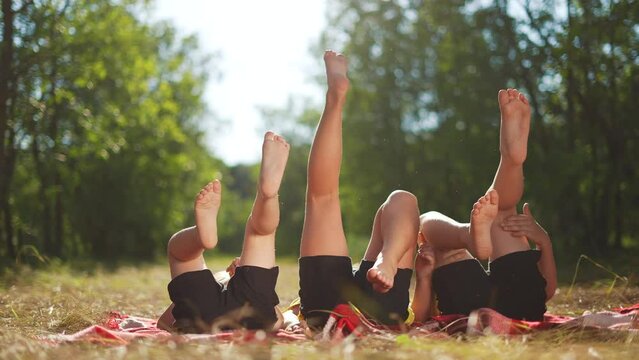 kid playing in the park. a group of children lie on their backs swinging their legs. happy family kid dream concept. happy family kids raised their feet up on fun nature in the park