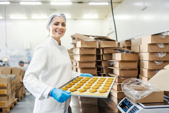 A Female Food Factory Worker Holding Tray With Fresh Cookies And Smiling At The Camera.