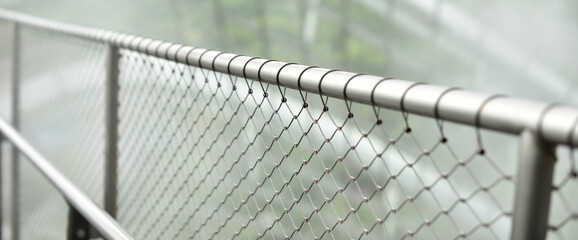 Silver metal fence with chain link in a tropical garden with a blur background.