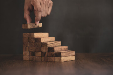 Hand is placing wood block tower stack in pyramid stair step with caution to prevent collapse or...