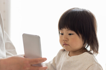 スマートフォン見る赤ちゃん（1歳8か月、女の子、日本人）と、見せる母親の手（30代、日本人）