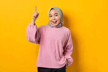 Shocked young Asian woman in pink shirt pointing fingers up having a good idea on yellow background