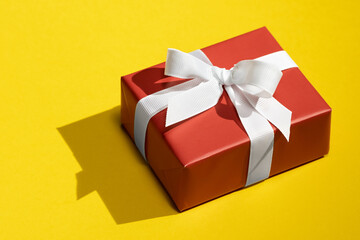 Red gift box tied with white ribbon on isolated on yellow background. Present box with white bow and ribbons. High Angle View Of Christmas Present Over yellow background. Holiday concept