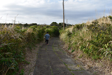 山の中の石畳の下り道をビニール袋に水筒を入れて持って歩く男性
