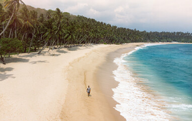 Podróżnik idący tropikalną plażą na tle palm i niebieskiego oceanu, piękny krajobraz.