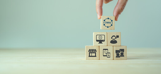 Omnichannel marketing concept. Digital online marketing commerce sale. For customer engagement by integrated online and offline channels. Hand holds wooden cube with omni text standing with omni icon