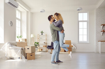 Happy young Caucasian couple renters hug celebrate relocating moving to new house together. Smiling...