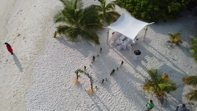 drone shot Beautiful Wedding event decoration beach sea tropical island maldives. Set up arch decor flowers pattern coconut palm trees sand sunlight. Setting outdoor marriage detail table stage 
