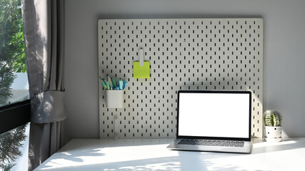 Laptop computer, potted plant and pegboard on white table. Blank screen for your text message or information content.