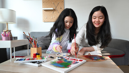 Obraz premium Adorable asian girls painting picture on canvas together at home.