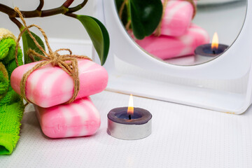 a stack of towels soap tied with string a fragrant candle a mirror and a houseplant on the bathroom table