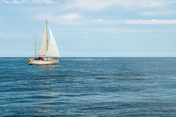 Veleiro com detalhes vermelhos e velas brancas navegando tranquilo em um mar calmo em um belo dia de sol
