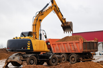 An excavator loads soil or sand into a dump truck. Pit development. Earthworks with the help of heavy construction equipment.