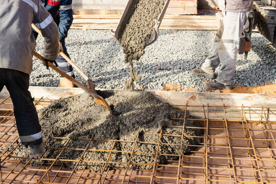 Pouring cement or concrete with a concrete mixer truck, construction site with a reinforced grillage foundation. Workers settle and level the concrete in the foundation.