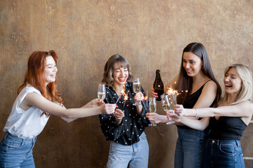 Group of young adult girlfriends drinking sparkling wine and firing sparklers, celebrating together...