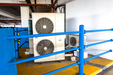 Large industrial units of air conditioners behind blue railings. Pipes and communications of the...