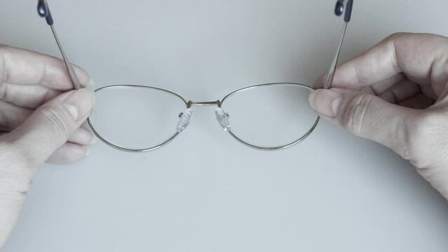 Close-up of a woman keeps reading glasses with diopters in her hands on a neutral background.