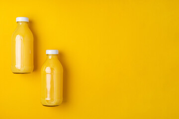 Two glass bottles with orange juice on a bright yellow background