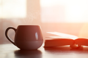 Cup of tea or coffee and open book on wooden table, morning background
