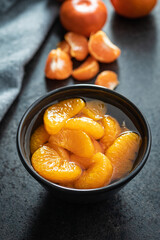 Canned tangerine. Pickled mandarin fruit in bowl on black table.