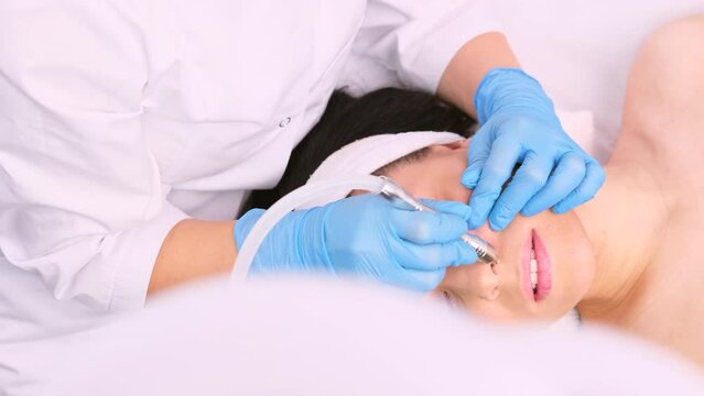 Professional cosmetologist doing rejuvenation procedure with a electric microdermabrasion vacuum massage instrument on woman nose.