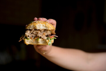 female hands holding a large hamburger on a dark background. A hamburger bitten off to see what's inside, the filling of a hamburger. I love hamburger. selective soft focus. space for copying.