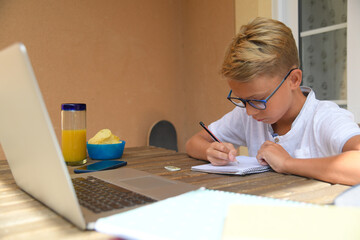 Student doing homework with books and laptop. Boy writing and drawing with pencil, sitting at the table outdoor. Creative young male write listening music. Lifestyle, school, youth, education concept.
