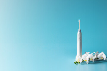 Modern ultrasonic toothbrush and white prchid flower on  blue gradient background.Copy space